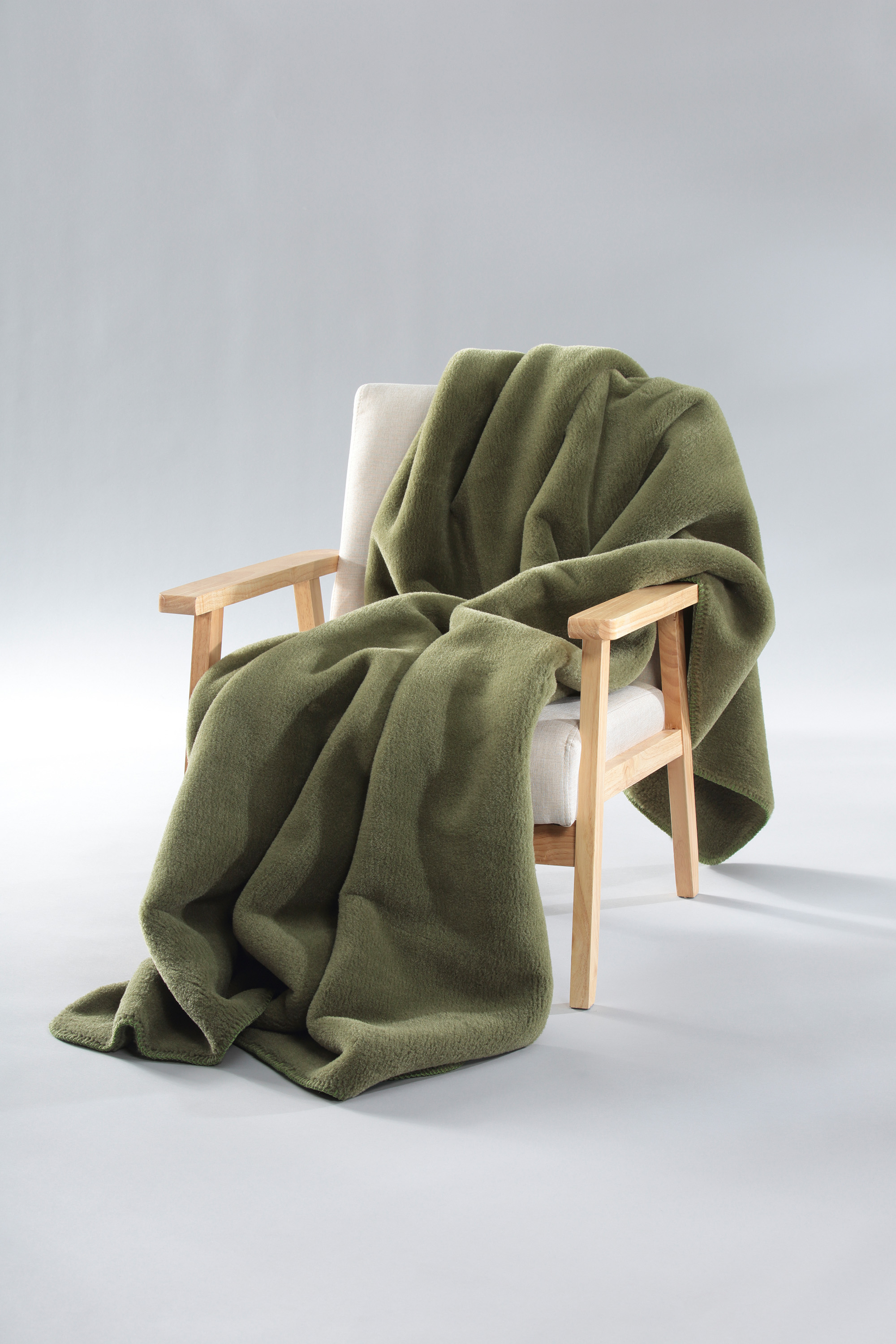 Wohndecke Wool Feel mossy auf Sessel gelegt